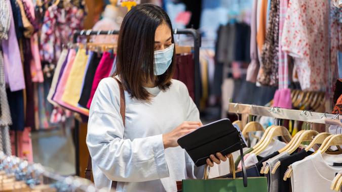 young woman open purse to payment for clothes at shopping store and her wearing medical mask for prevention from coronavirus (Covid-19) pandemic.