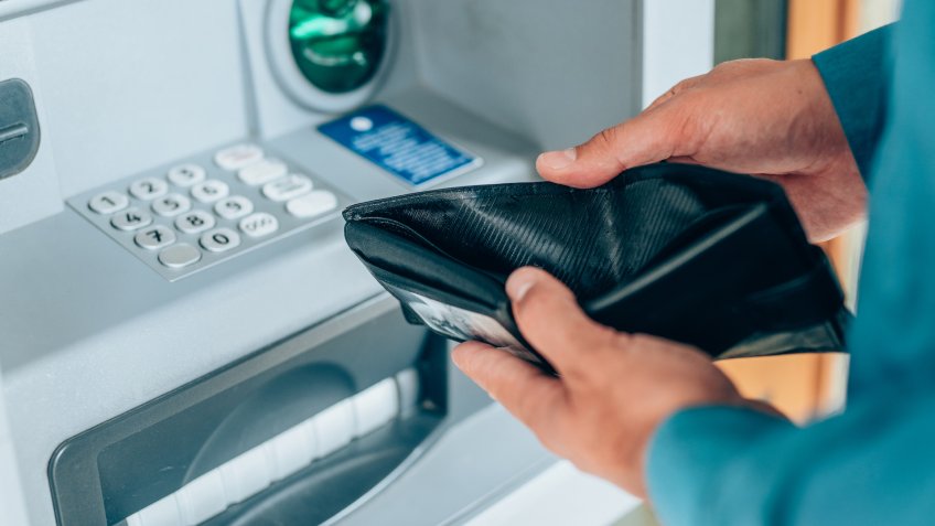 Man standing with empty wallet in the hands in front of ATM.