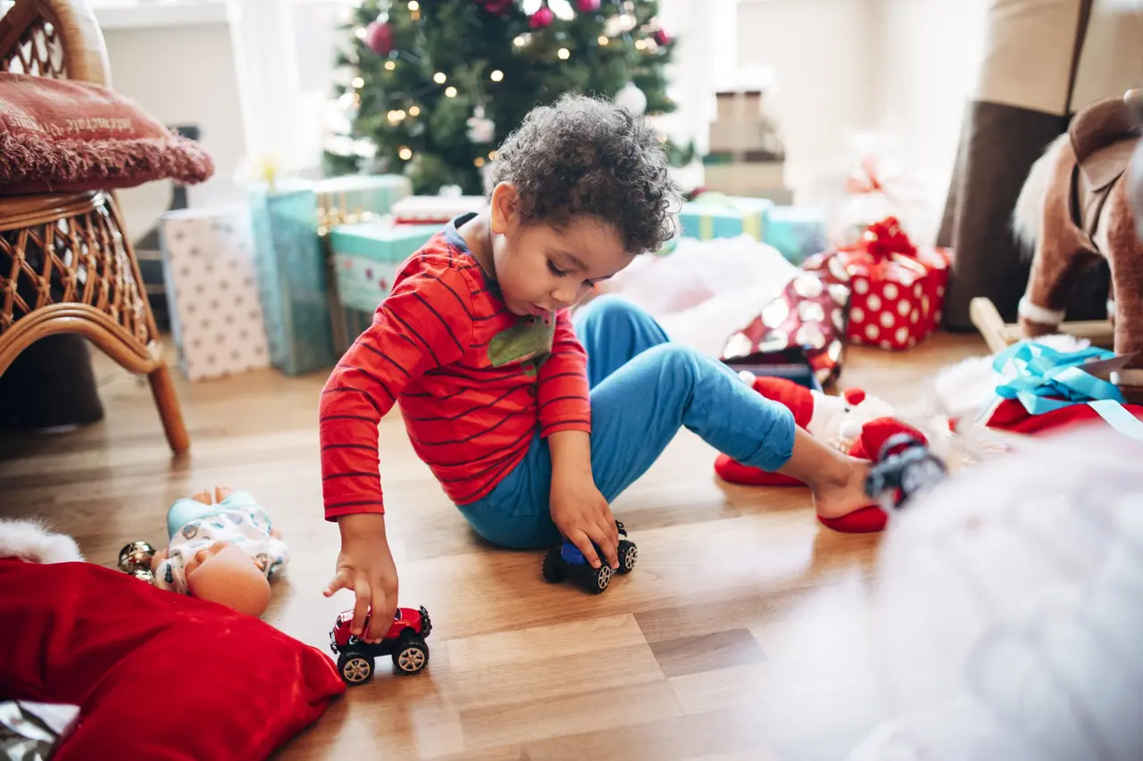 A little boy plays with some toy cars he has received as a Christmas present in front of the Christmas tree.