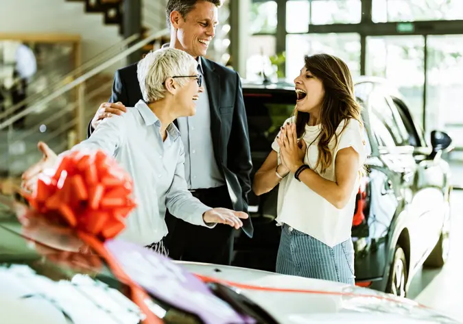 Young cheerful daughter feeling surprised after her parents bought her a car in a showroom.