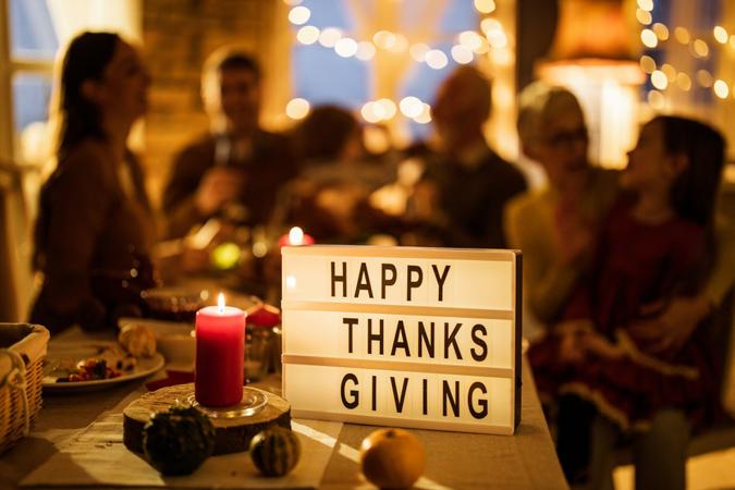 Close up of a candle and sign with 'Happy Thanksgiving' on dining table with people in the background.