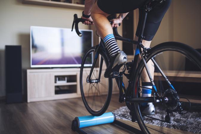 Unrecognizable man cycling indoor with exercise bike trainer.