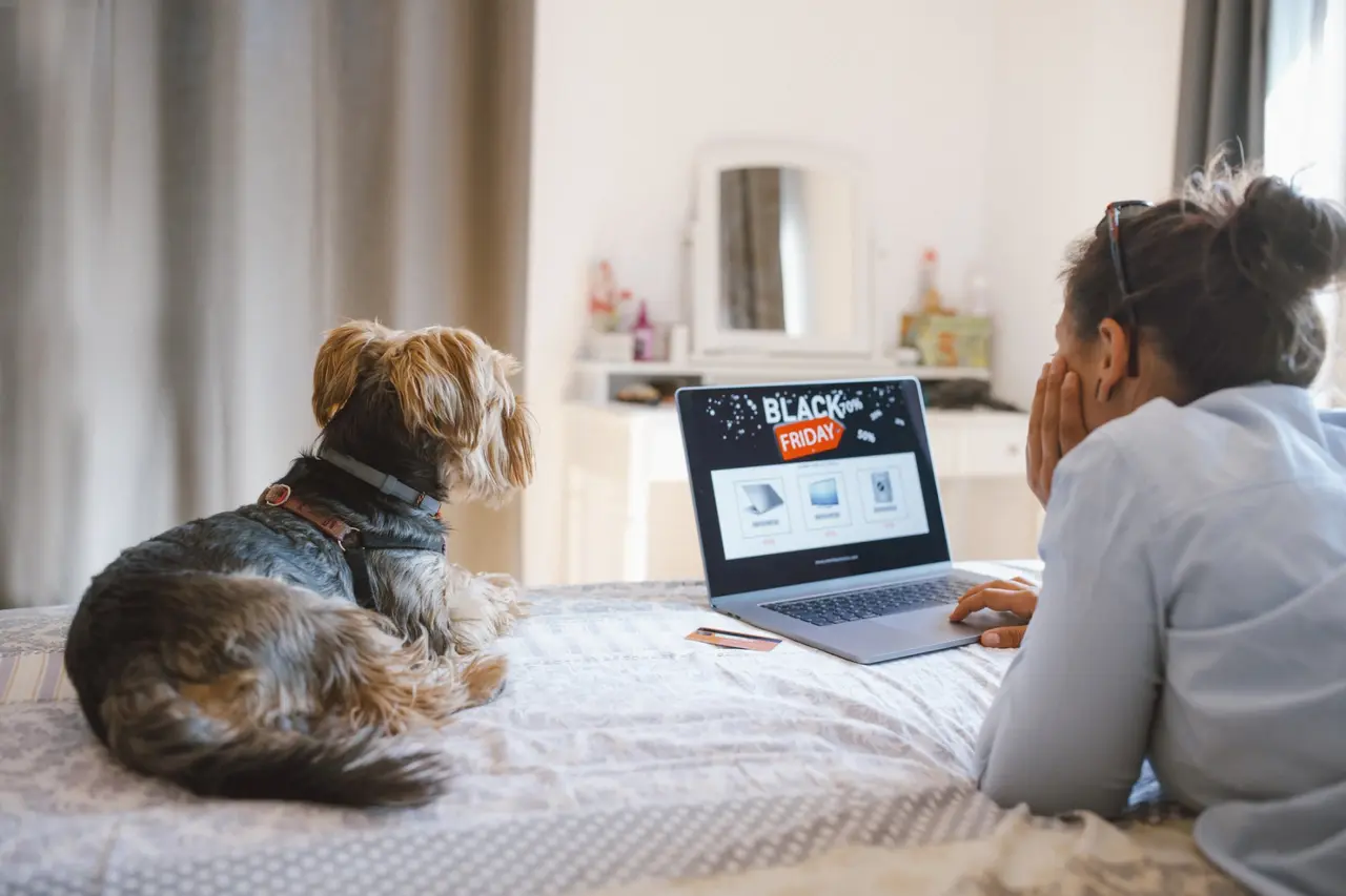 Woman is buying electronics online at Black Friday while relaxing at the bed with her dog.