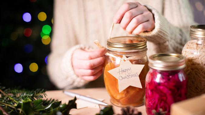 Putting Reusable Wooden Gift Tag On Homemade Jars Of Preserved Fruit For Eco Friendly Christmas Gift.