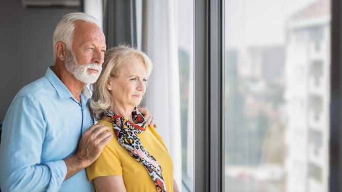 Worried senior couple looking at view through window of their home.