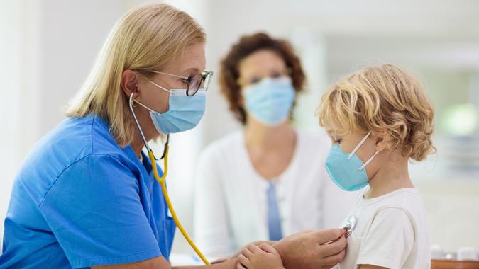 Pediatrician doctor examining sick child in face mask.