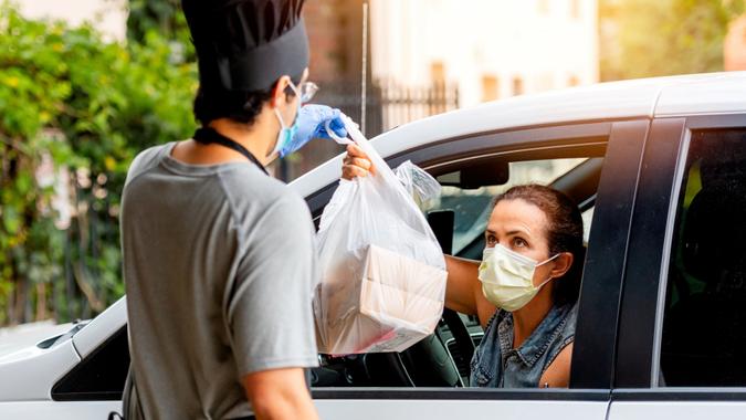 Caucasian mature woman picking her restaurant food from her car at a pick up curve.