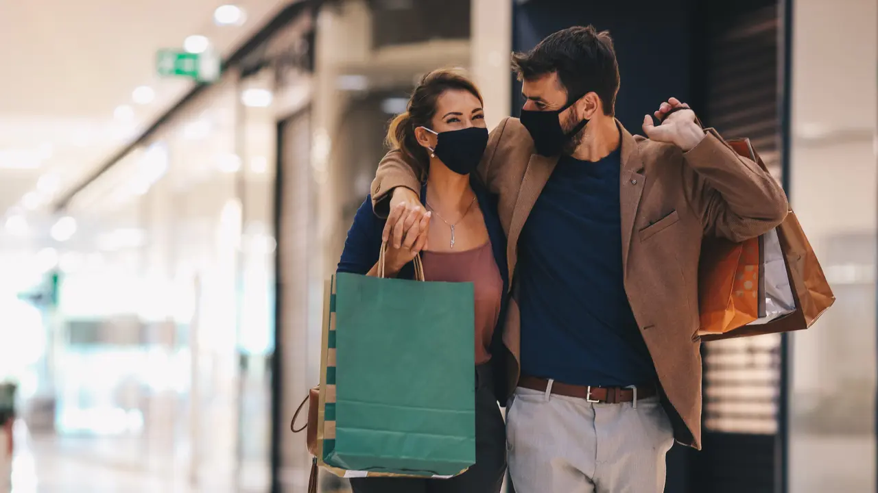 The young couple carries shopping bags and walks through the mall, wearing protective masks, life in a time of pandemic.