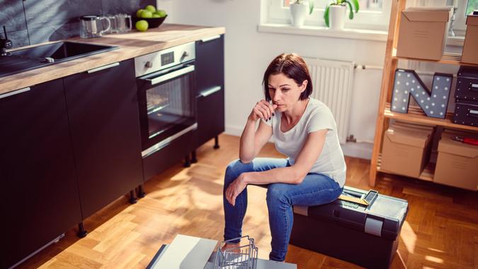 Worried woman sitting on a toolbox during renovating kitchen.