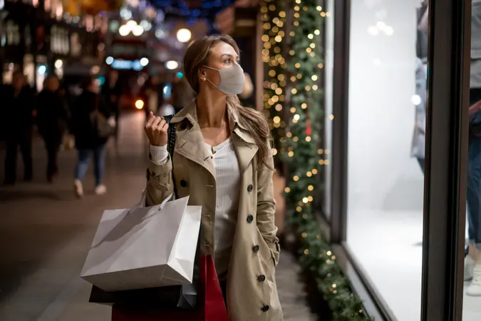 快乐的圣诞购物的女人戴着面罩和观察窗手里拿着购物袋。