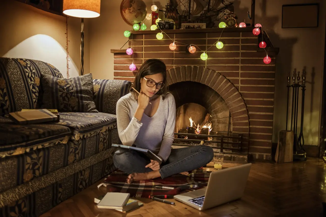 young woman studying in her cozy room,sitting on the carpet,next to the fireplace.