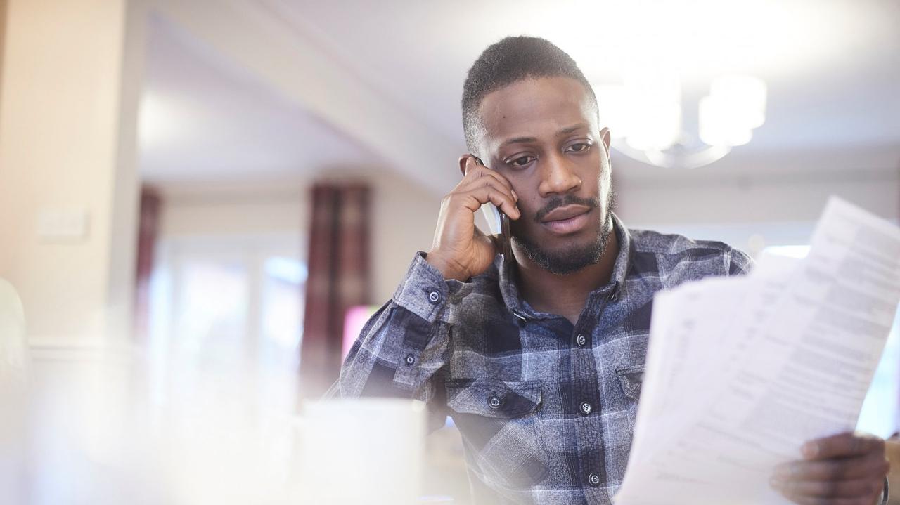 Young black male on the phone in a home environment holding paperwork.