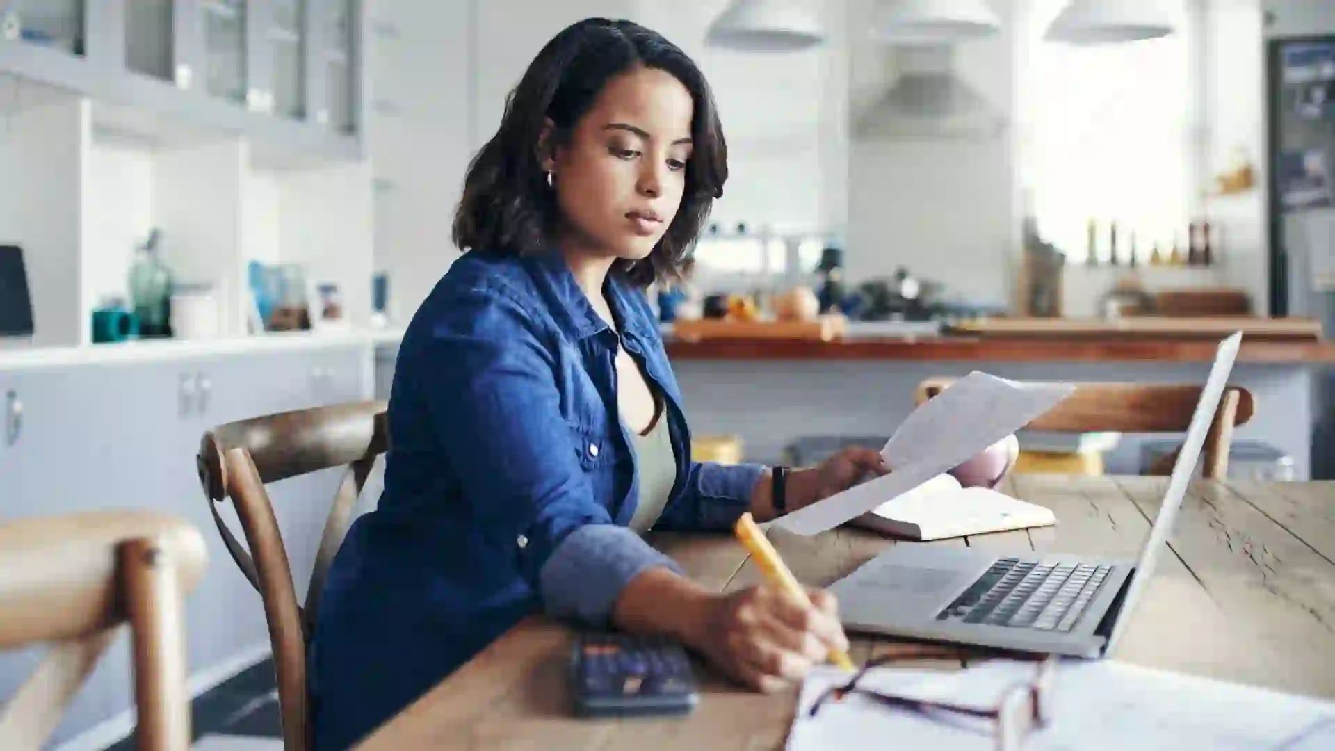 Shot of a young woman sitting and using a laptop and going through paperwork while working from home.
