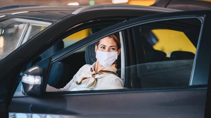 Young attractive elegant businesswoman with protective face mask on exiting car during corona virus outbreak.