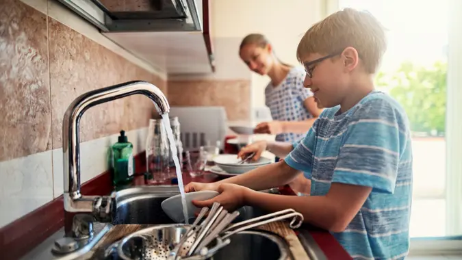 Three kids washing up dishes in kitchen.