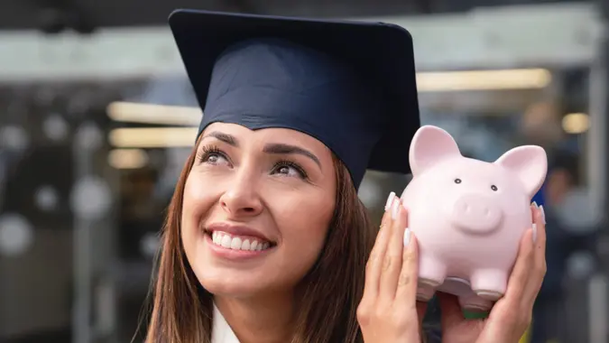 Portrait of a thoughtful graduate student saving for her education and holding a piggybank.