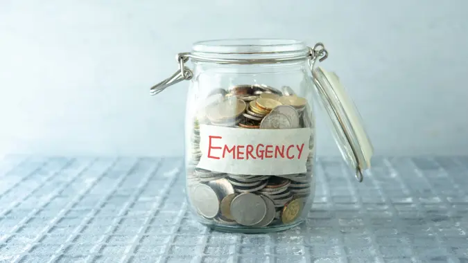 Coins in glass money jar with emergency label, financial concept.