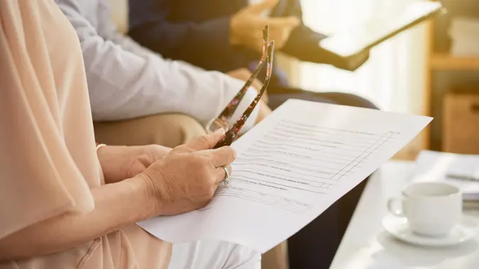 Close-up shot of senior husband and wife sitting at cozy office and studying life insurance policy, female agent assisting them.