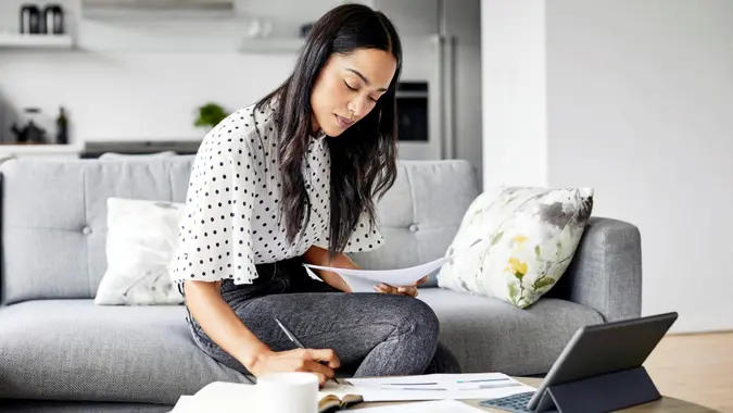 Young woman analyzing bills while writing in diary.