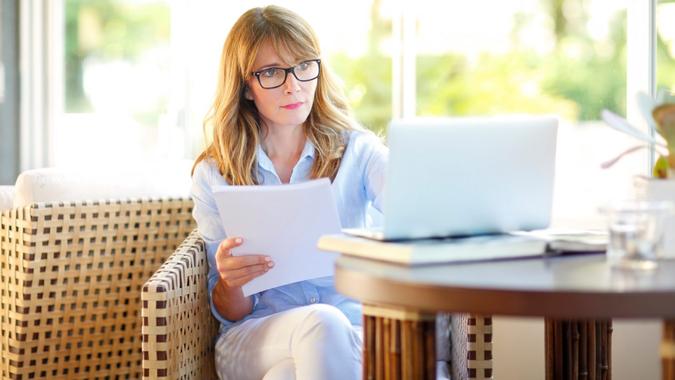 Portrait of confident businesswoman doing some paperwork and using laptop while working at coffee shop.