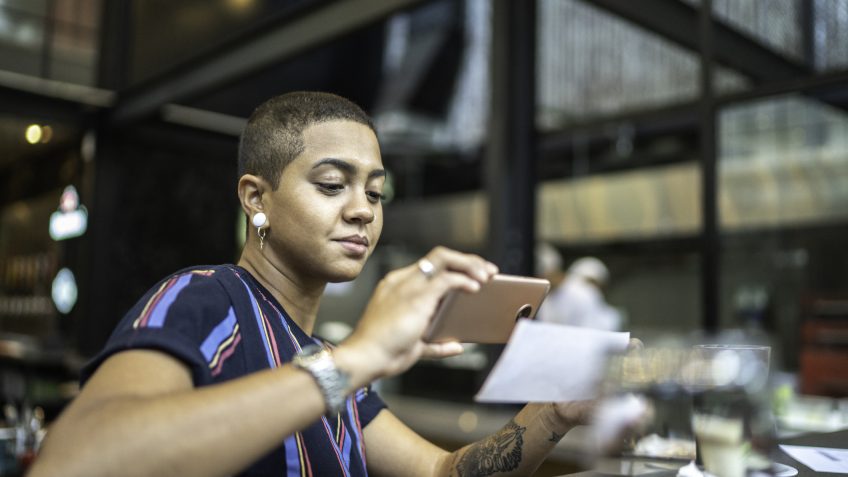 Young woman depositing check by phone in the cafe.