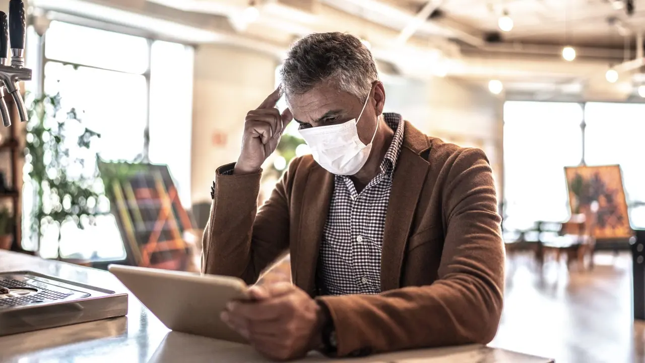 Mature businessman with mask using digital tablet at work.