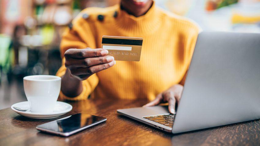 Cropped shot of young african-american woman shopping online in cafe using laptop and credit card.