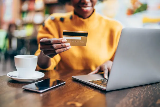 Cropped shot of young african american woman shopping online at cafe using laptop and credit card.