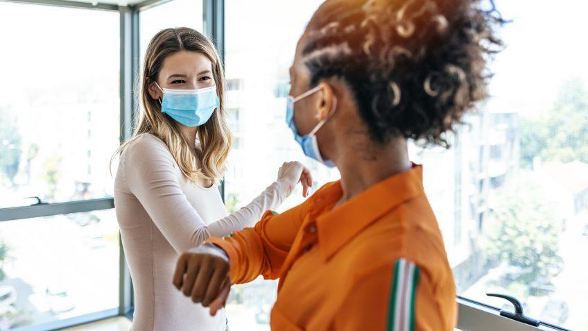 Two colleagues in medical masks avoiding handshake when meeting in the office, greeting with bumping elbows during corona virus COVID-19 epidemic in office, Social distancing concept.