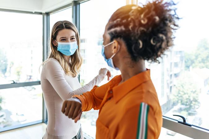 Two colleagues in medical masks avoiding  handshake when meeting in the office, greeting with bumping elbows during corona virus COVID-19 epidemic in office, Social distancing concept.
