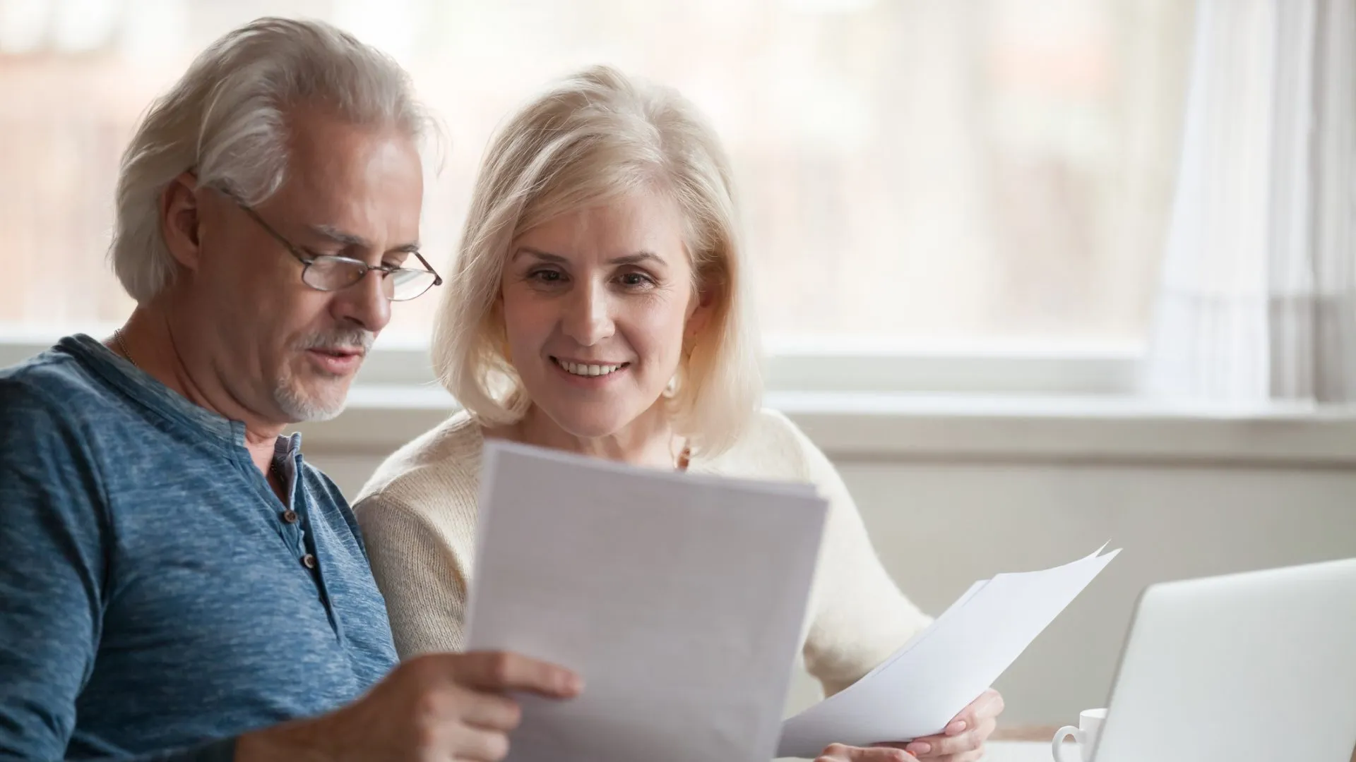 快乐的中年老夫妇抱着阅读文件中的好消息，微笑的年长成熟的家庭兴奋的邮件信件，在笔记本电脑上查看在线支付家庭账单，讨论预算计划。