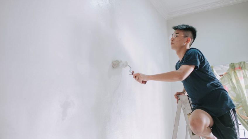 An asian chinese teenage boy painting his bedroom, apartment renovation during sunset.