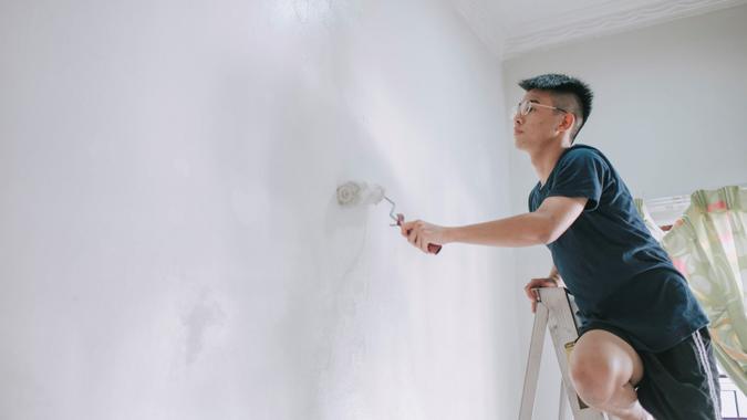 An asian chinese teenage boy painting his bedroom, apartment renovation during sunset.