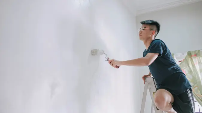 An asian chinese teenage boy painting his bedroom, apartment renovation during sunset.