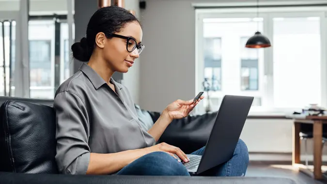 Young woman making online payment while sitting in the living room on sofa.