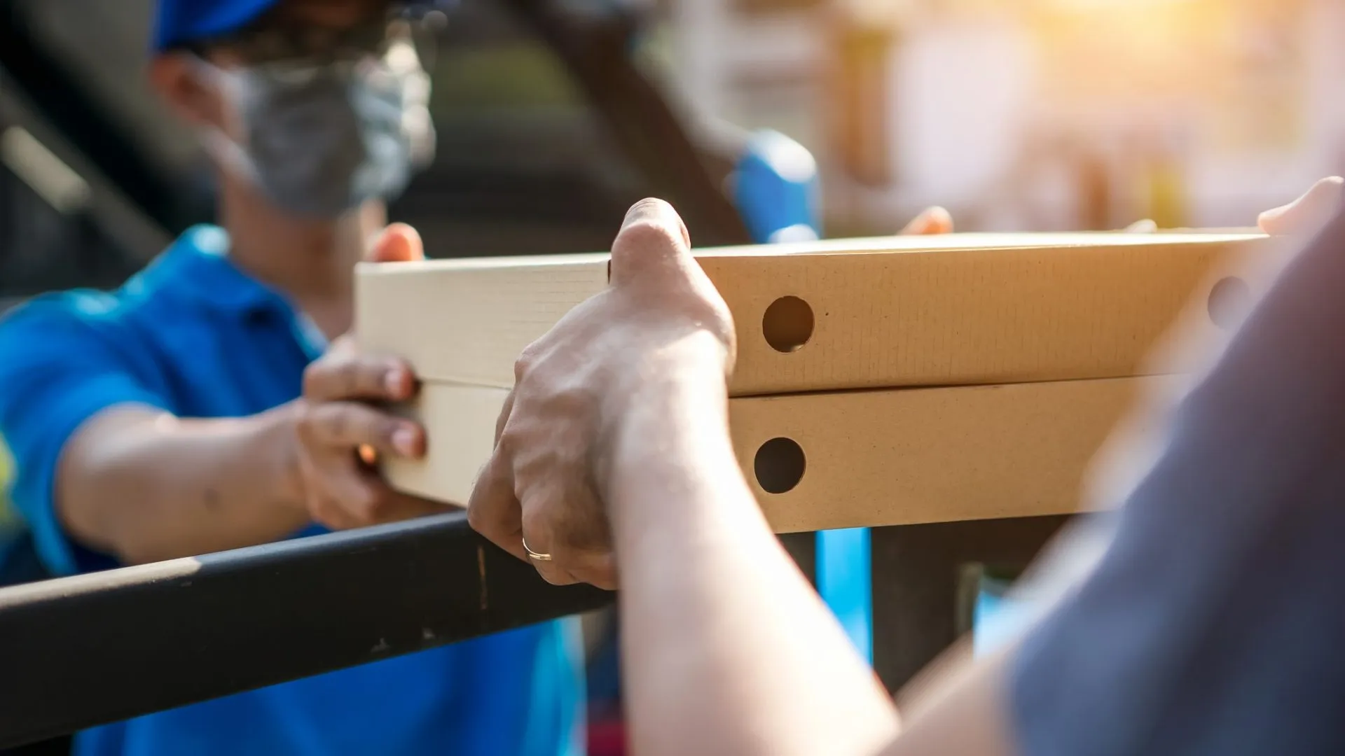 Asian delivery man wearing mask delivers pizza, customer in medical gloves signs on tablet.