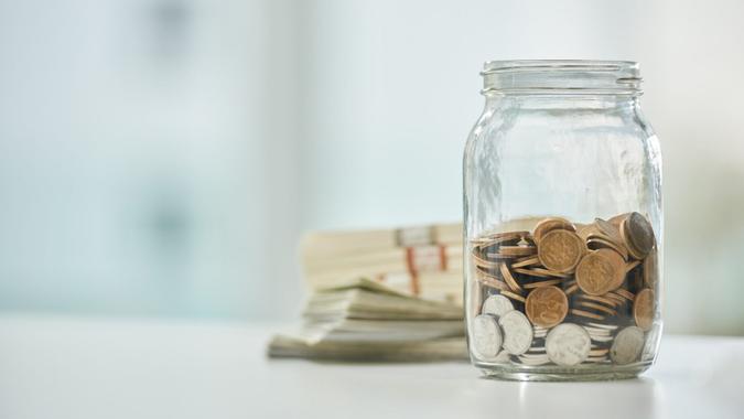 Full length shot of a jar of coins and wads of cash on a desk in an office.