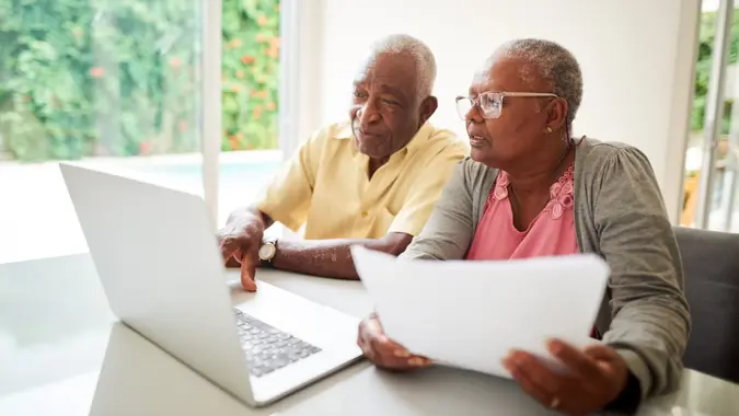 Shot of a senior african couple with a paper looking at a laptop at home.