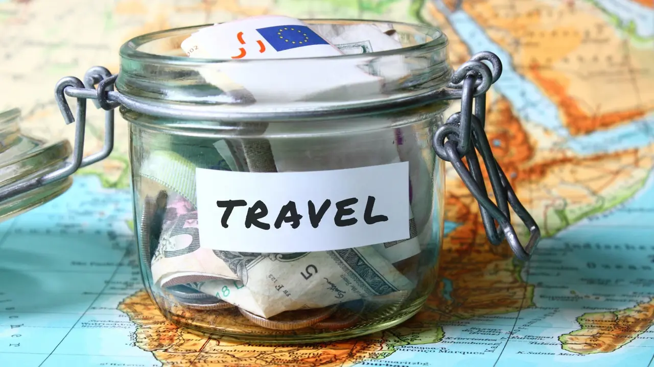 Travel budget - vacation money savings in a glass jar on world map.