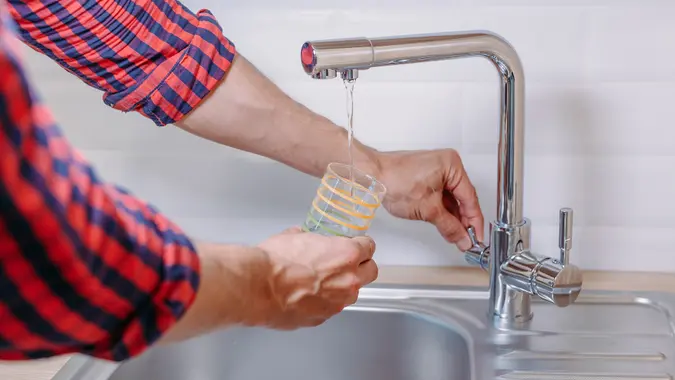 Man pouring glass of water from tap with clean filter in kitchen, close up stock photo
