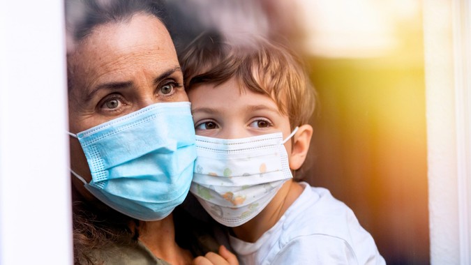 Caucasian Mature woman posing with her son, both with protective masks, very sad looking through window worried about loss of her job due Covid-19 pandemic.