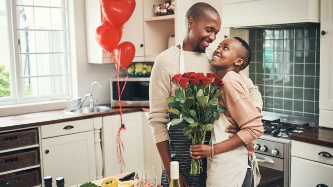 Cropped shot of an affectionate young couple posing with a bunch of flowers in their kitchen on their anniversary.