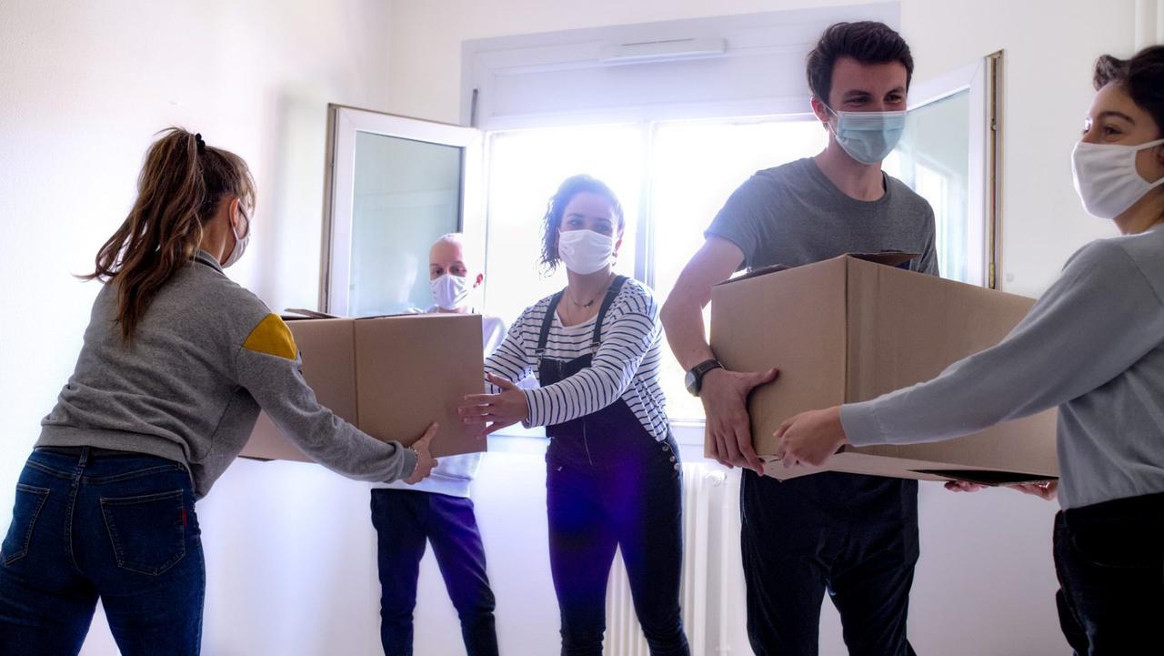a group of young people carry moving boxes in a room of an apartment.