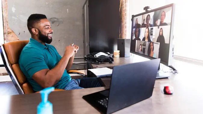 A mid adult businessman smiles confidently as he talks with a team of associates during a virtual meeting during the COVID-19 pandemic.