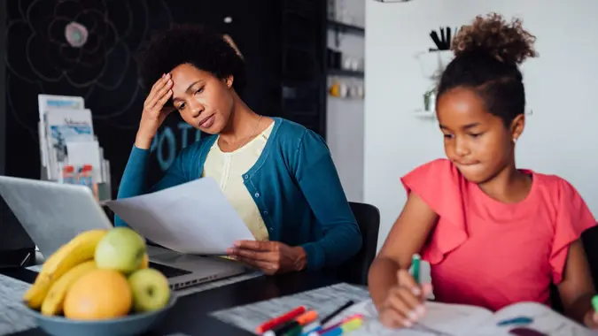 Young African American mother looking for a job using the laptop and struggling while her daughter is being home schooled due to the lack of income.