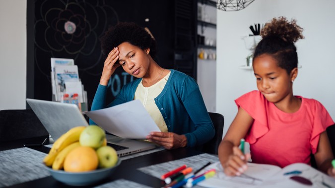 Young African American mother looking for a job using the laptop and struggling while her daughter is being home schooled due to the lack of income.