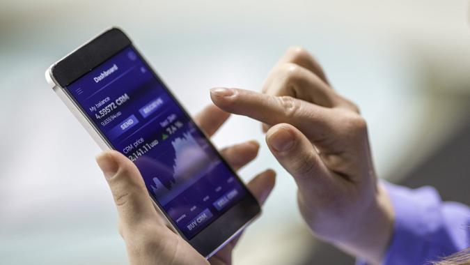 Close-up photo of a woman buying cryptocurrency through a smart phone app that is also showing the growth graph.