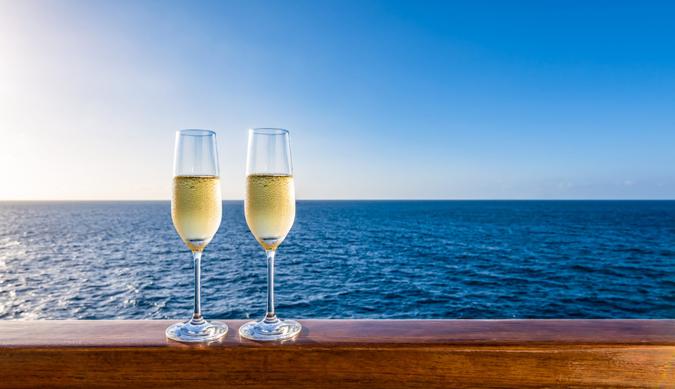 Side view of two glasses of sparkling wine on a wooden railing of a cruise ship.