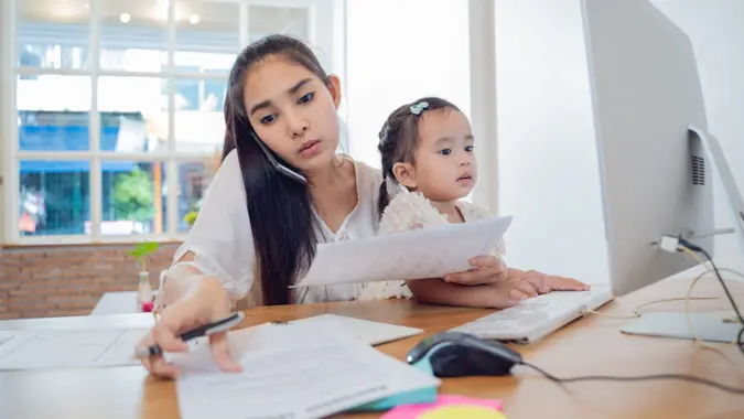 Working Parents at home,Busy Asian Woman mom working with Daughter at house.