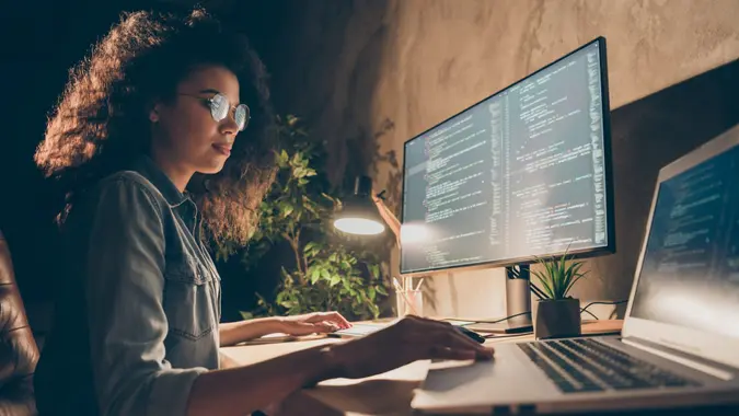 Profile side photo of concentrated skilled web expert afro american girl sit evening, desk use computer netbook work java script html back-end algorithm in workstation workplace.